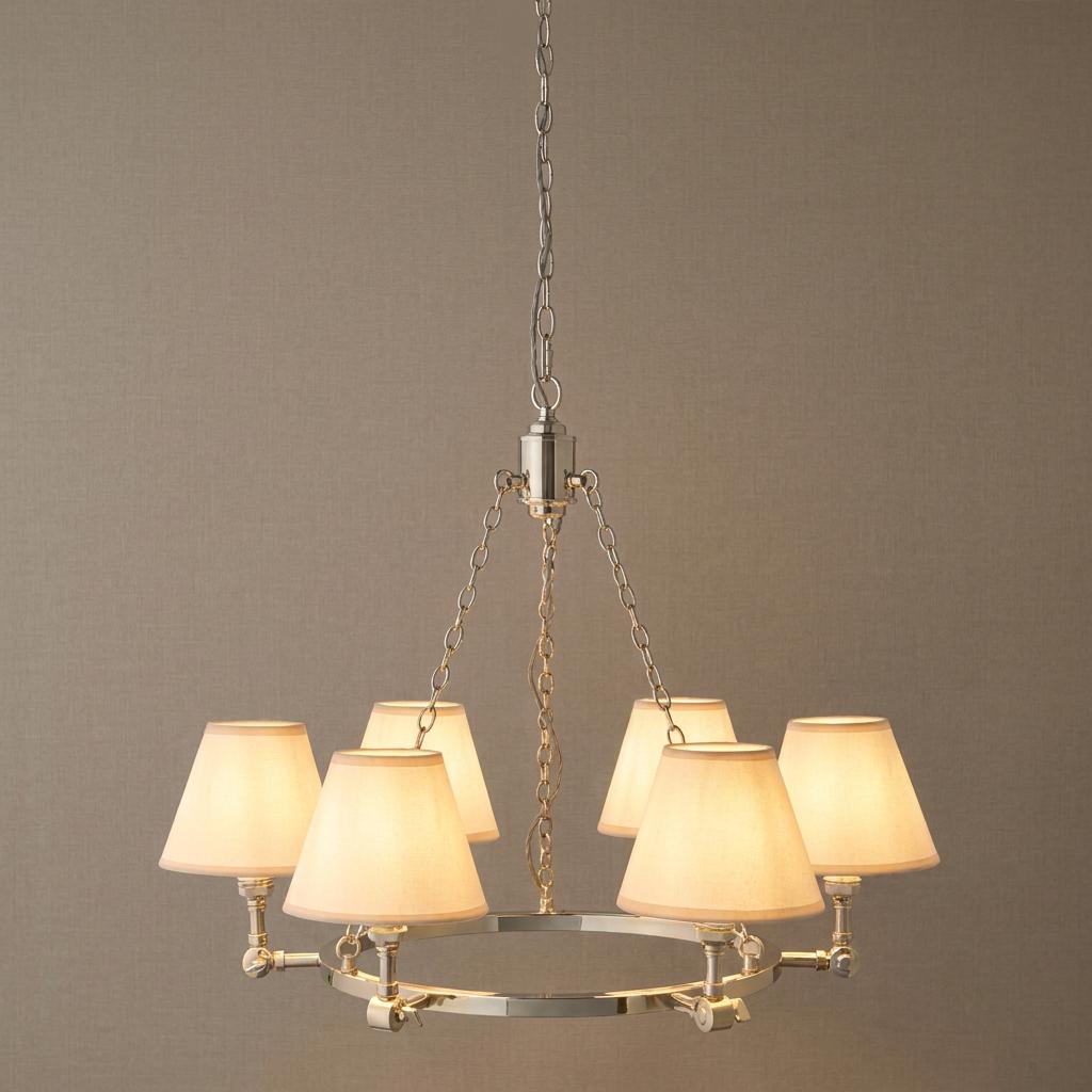 A five-light bright nickel chandelier with cream fabric shades suspended by a chain against a textured neutral wall.