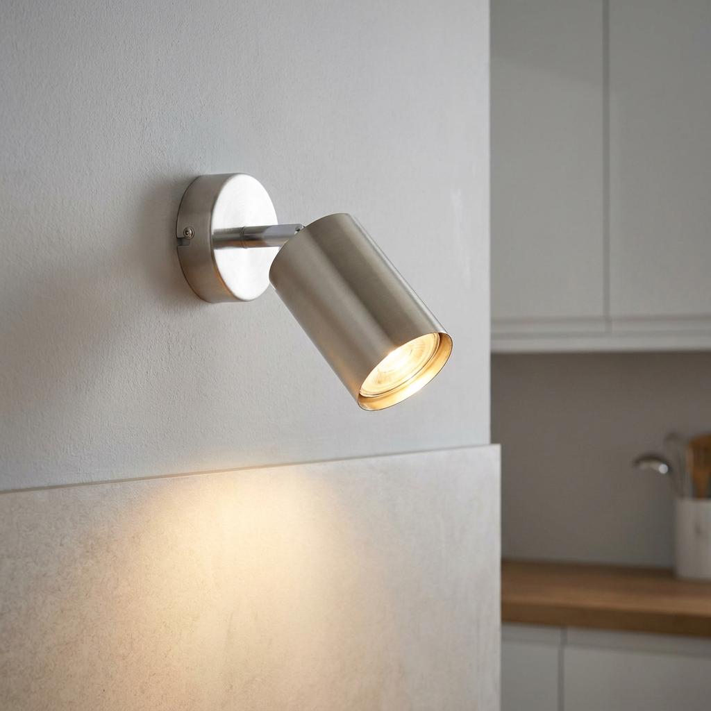 Arezzo satin chrome adjustable spotlight mounted on a kitchen wall, casting a warm glow downwards.