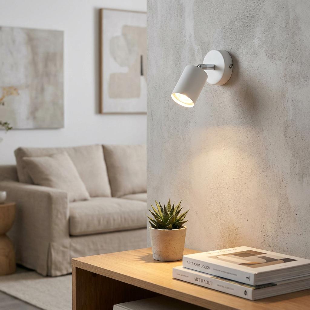 A white adjustable spotlight mounted on a textured wall, illuminating a succulent on a wooden table in a living room.