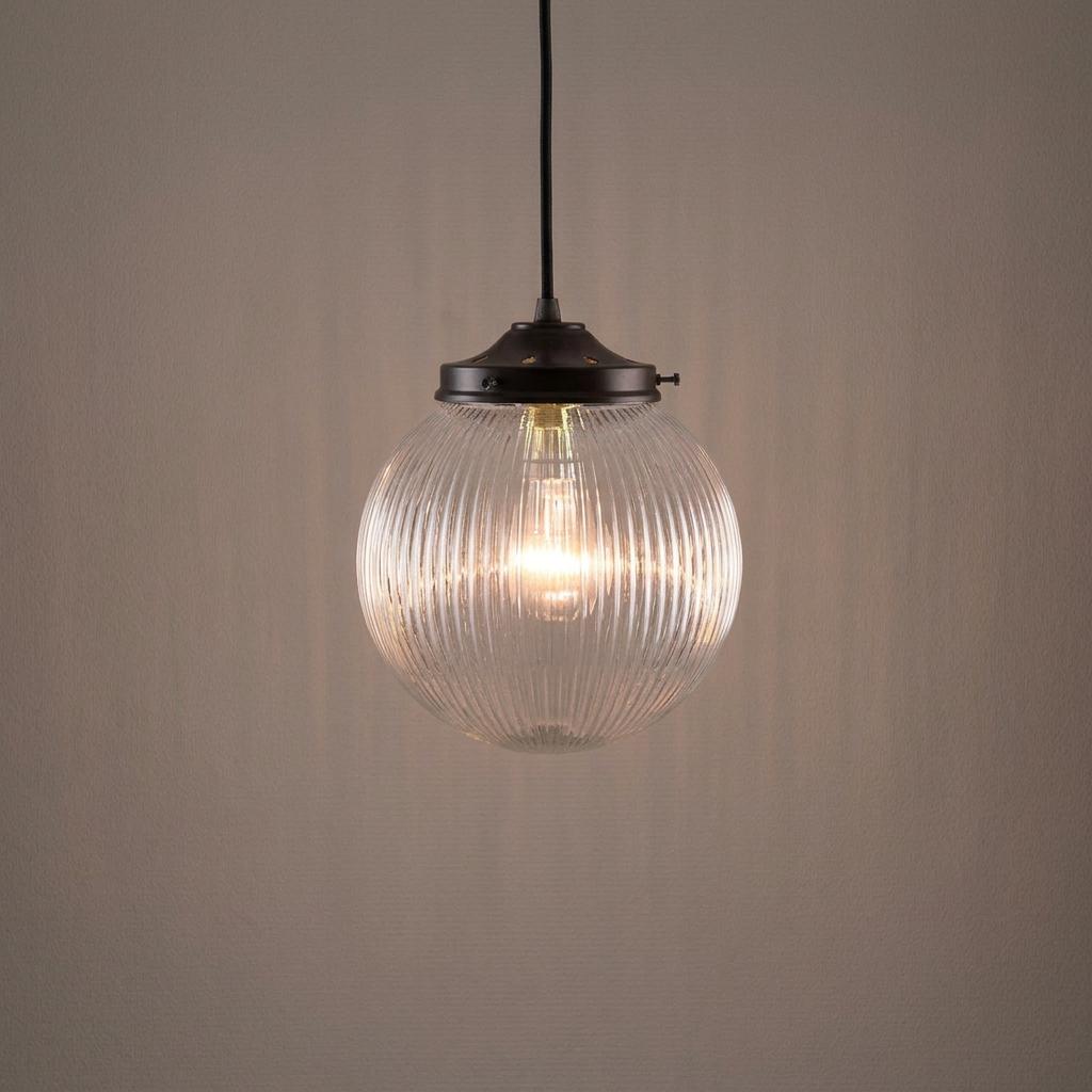 Illuminated prismatic glass globe pendant light with a dark metal fixture hanging against a plain wall.