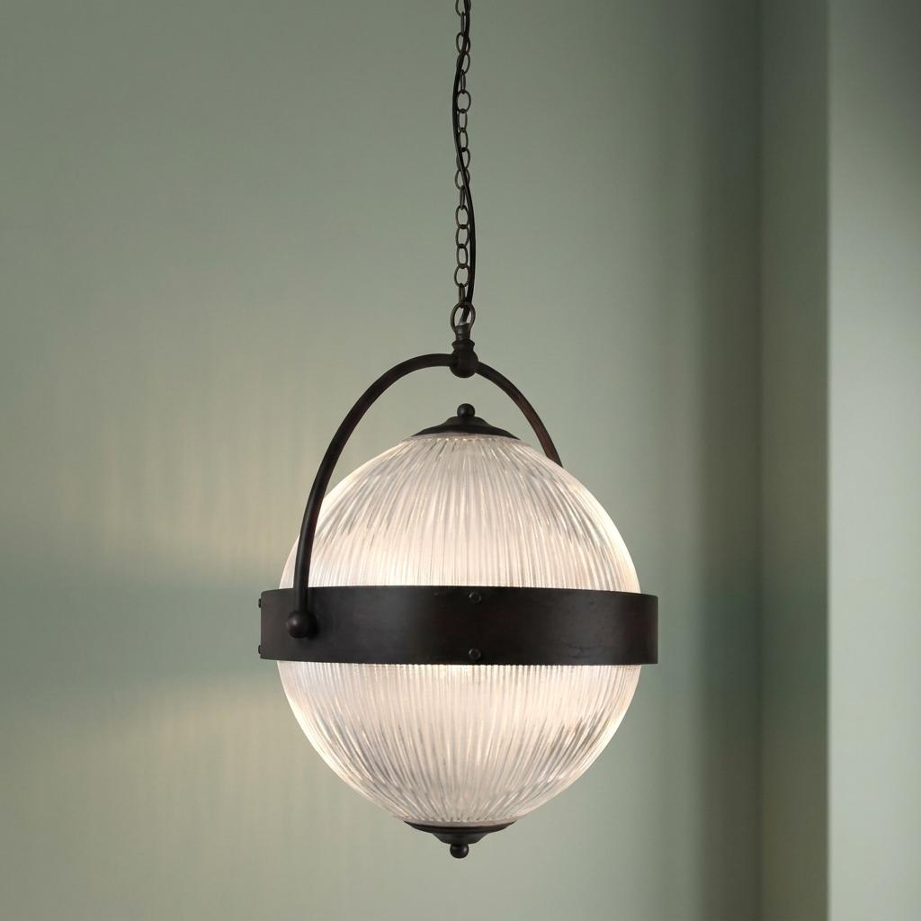 A glowing Art Deco prismatic glass globe pendant light with a dark bronze metal frame against a pale green wall.