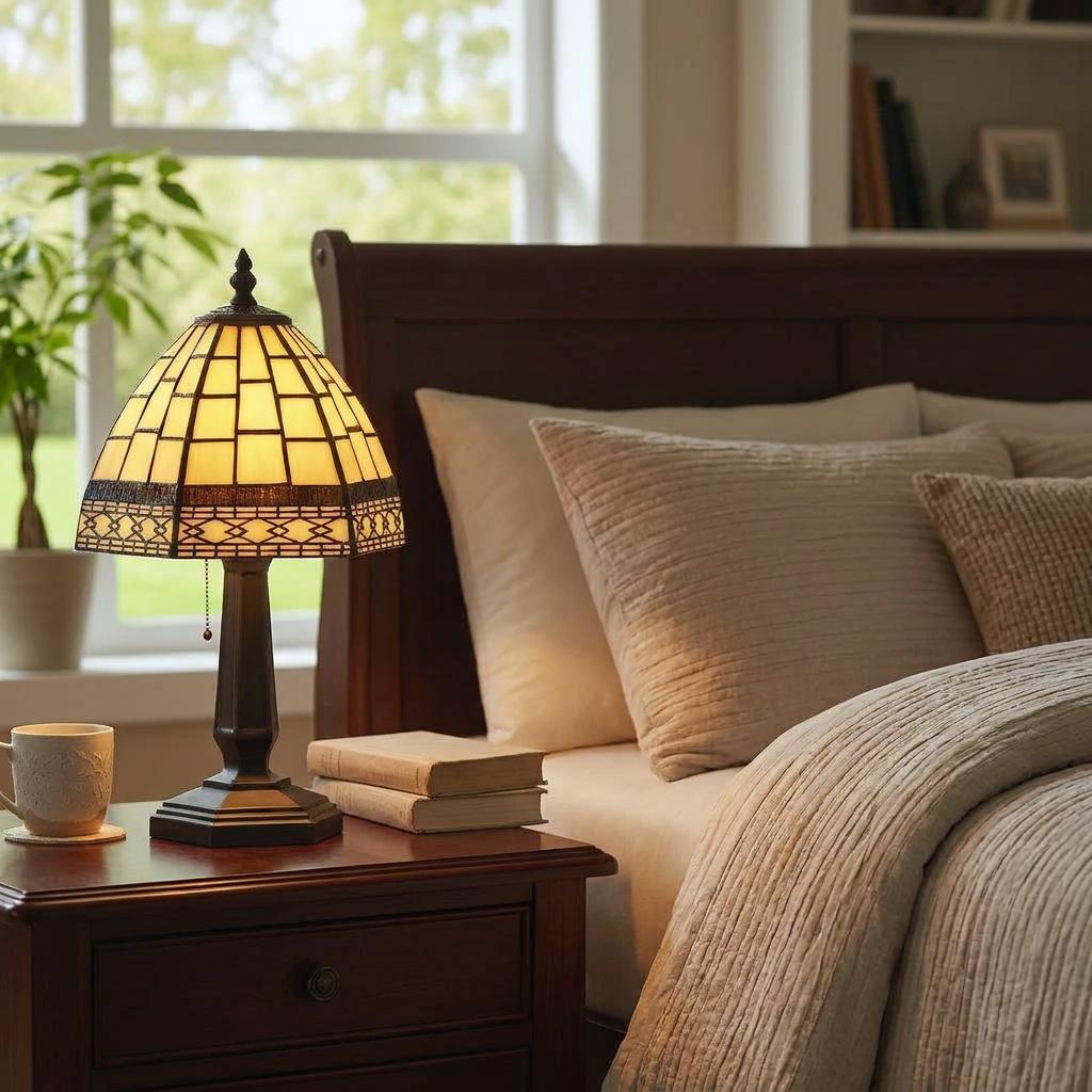 An illuminated cream Art Deco Tiffany lamp on a wooden bedside table in a cozy, neutral-toned bedroom.