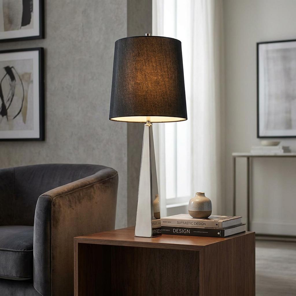 Modern table lamp with a polished nickel obelisk base and black fabric shade on a wooden side table.