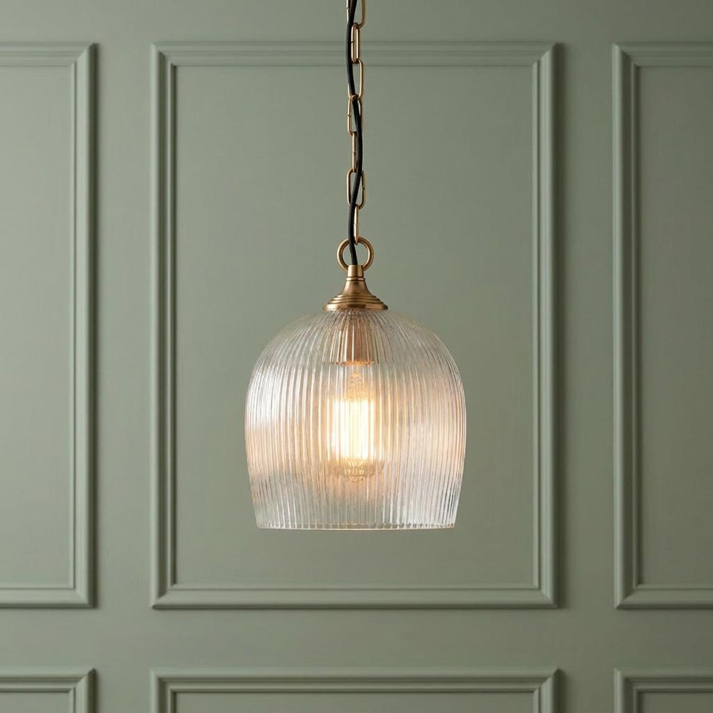 A lit Ashcroft ribbed glass shade brass pendant light hangs against a sage green paneled wall.