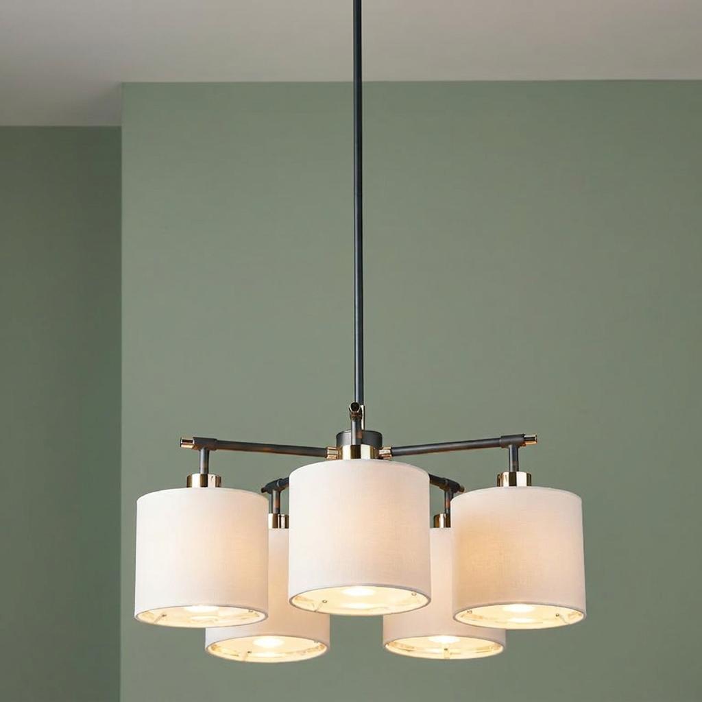Five-light black chandelier with white fabric shades and gold accents hanging against a sage green wall.