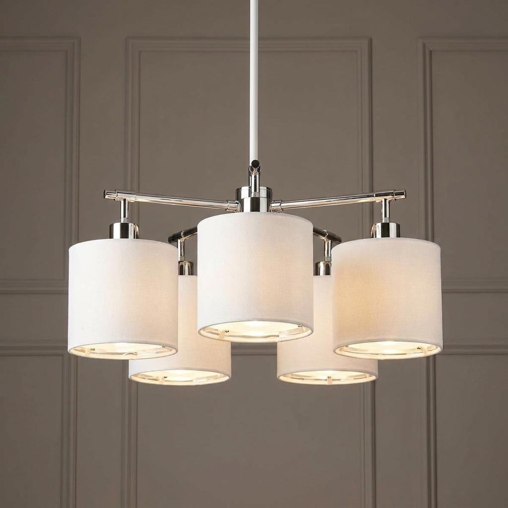 Modern five-light chandelier with white fabric drum shades and polished nickel accents against a neutral wall.