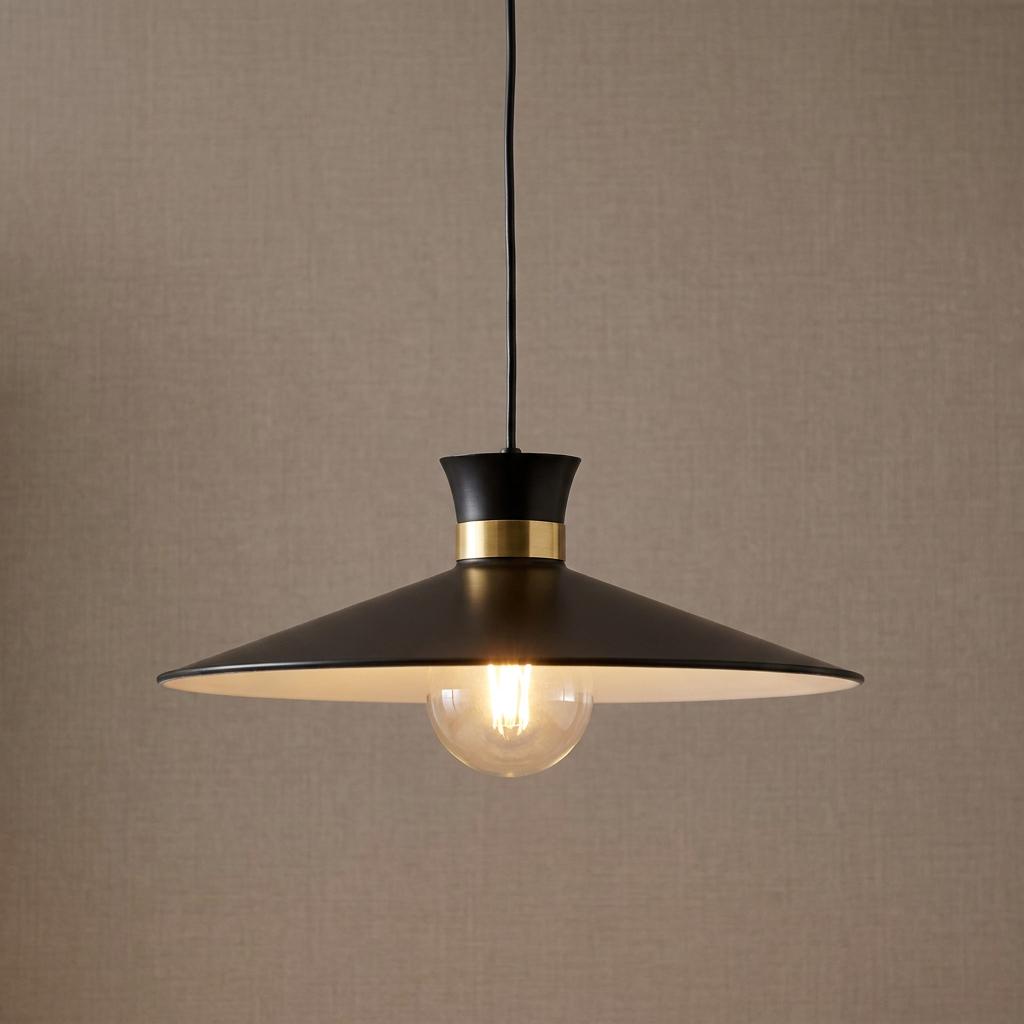 Modern black pendant light with a brass collar and exposed bulb against a textured beige wall.