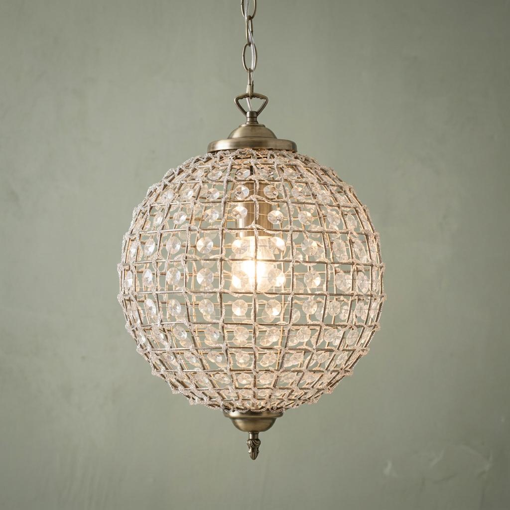 Antique brass globe pendant light with clear crystal beads in a mesh frame, hanging against a sage green wall.
