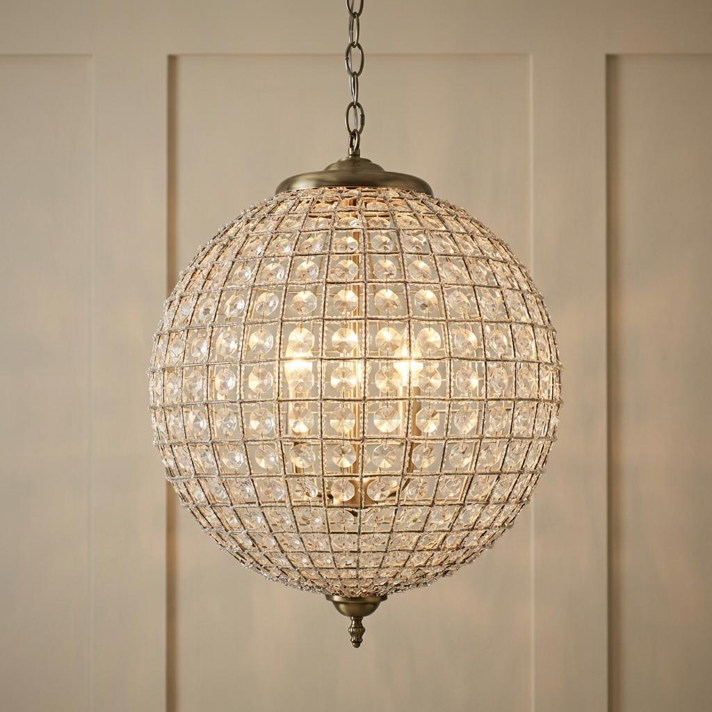 A glowing 45cm crystal globe pendant light with antique brass accents hanging against a neutral paneled wall.