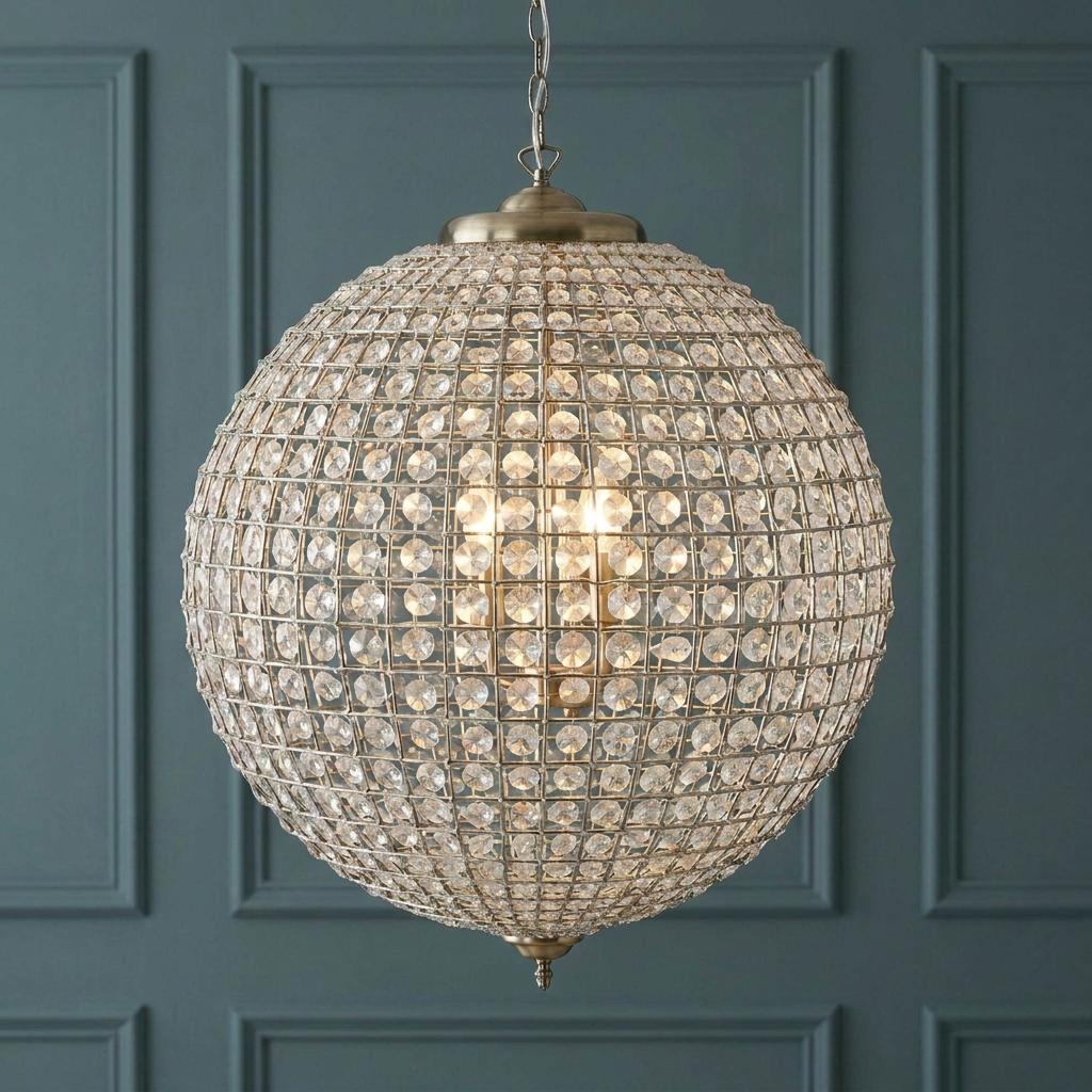 Ballon antique brass and crystal globe pendant light illuminated against a blue decorative wall.