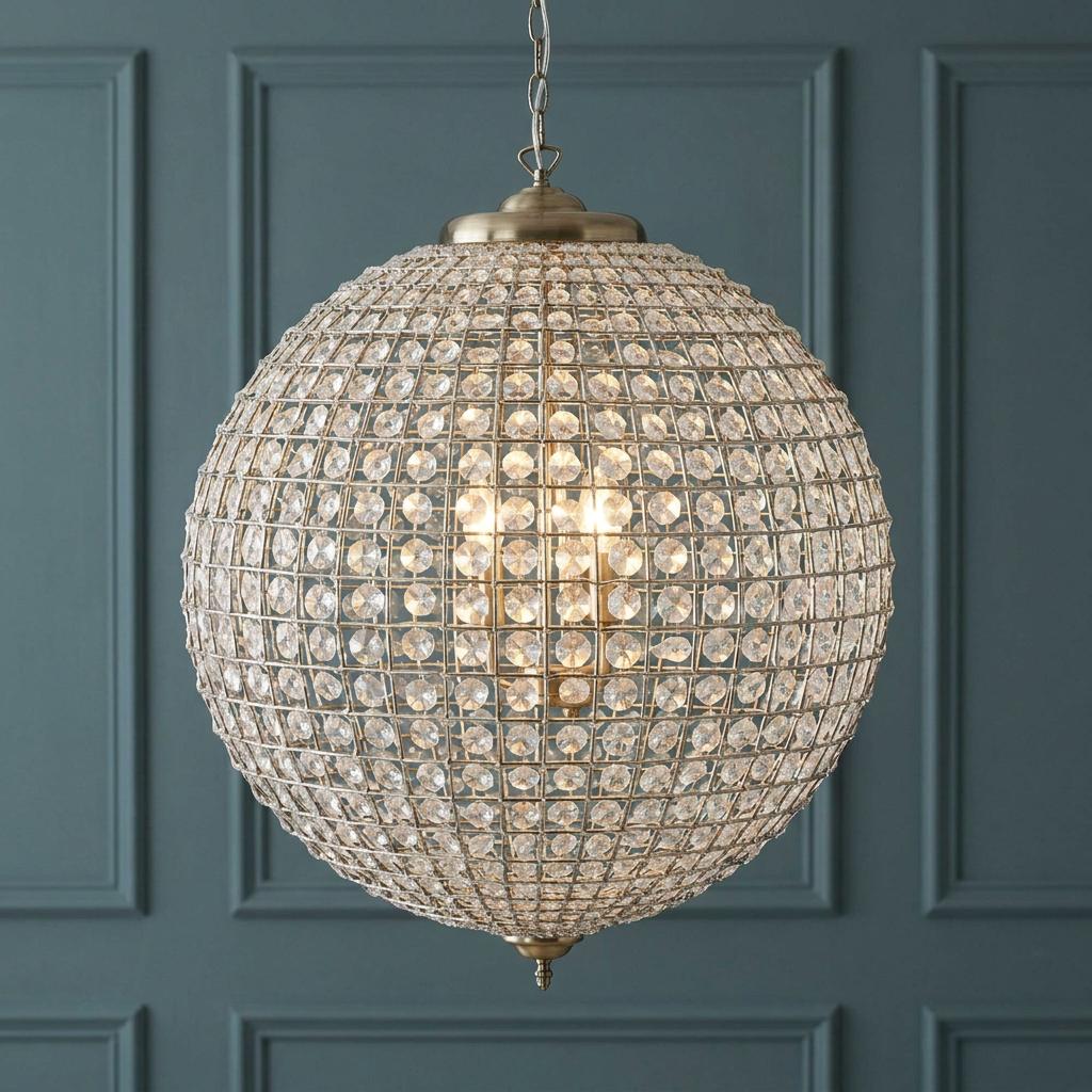 A 60cm crystal globe pendant light with antique brass frame hanging against a teal paneled wall.
