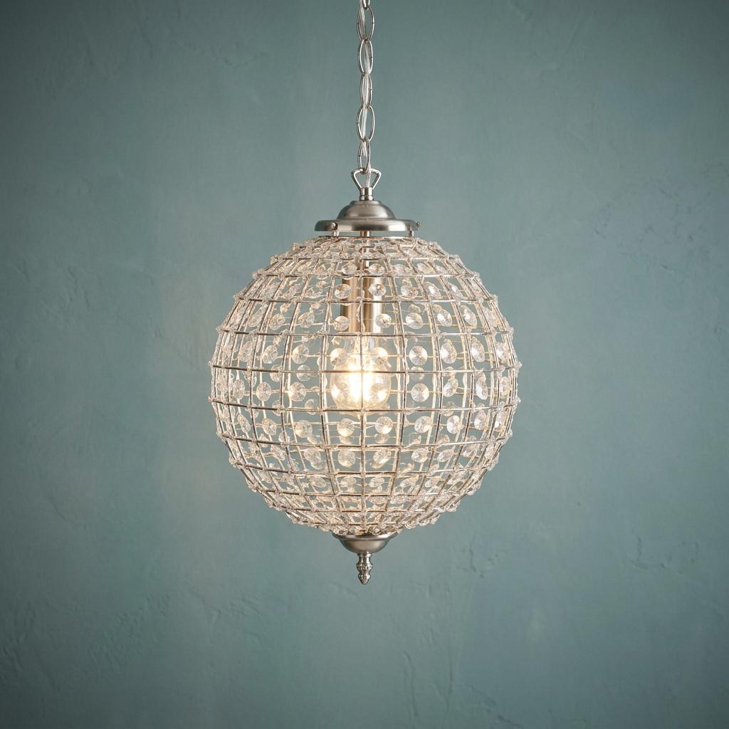 Spherical antique chrome pendant light with clear acrylic beads, lit from within against a teal wall.