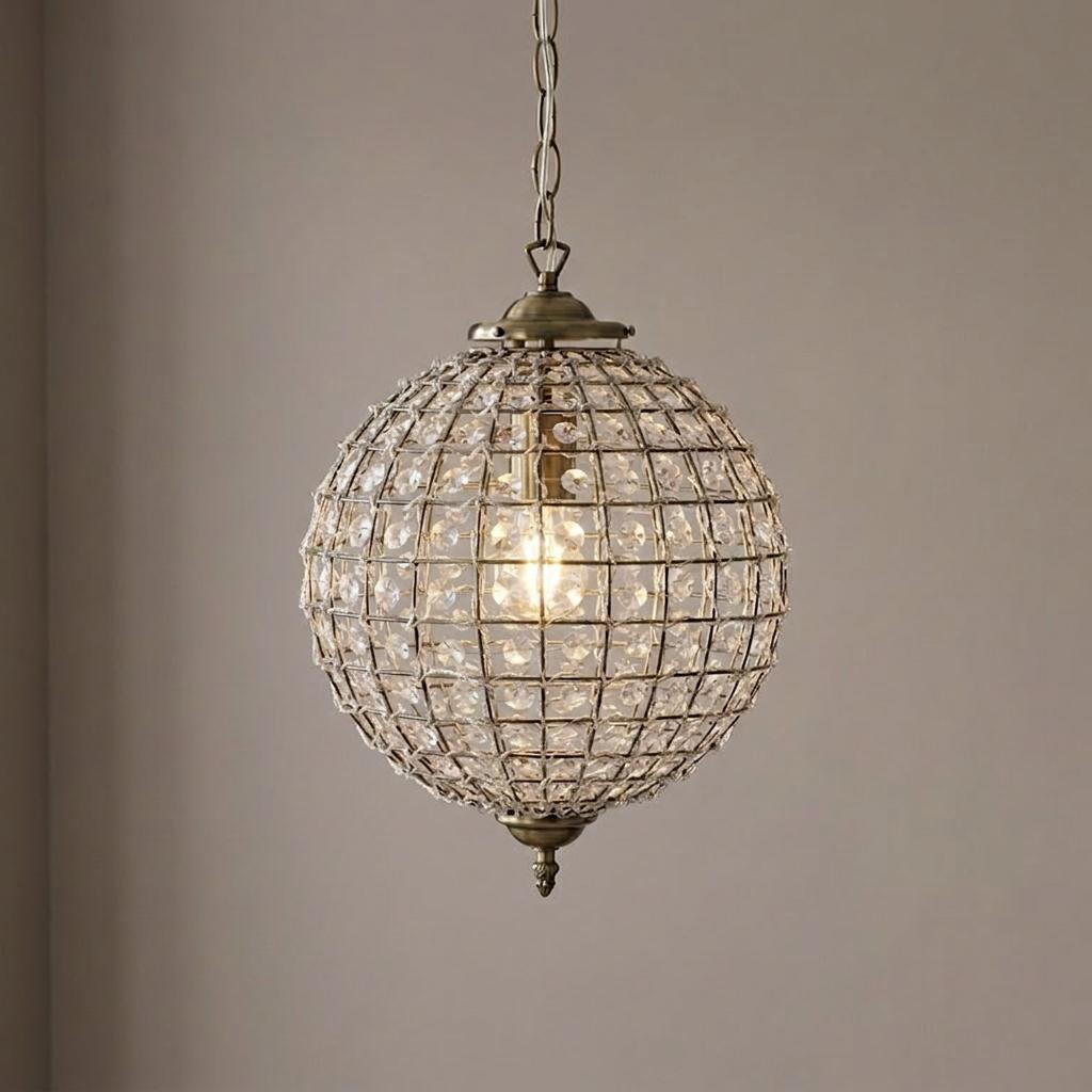 Antique brass spherical pendant light with a clear acrylic beaded cage and an internal glowing bulb.