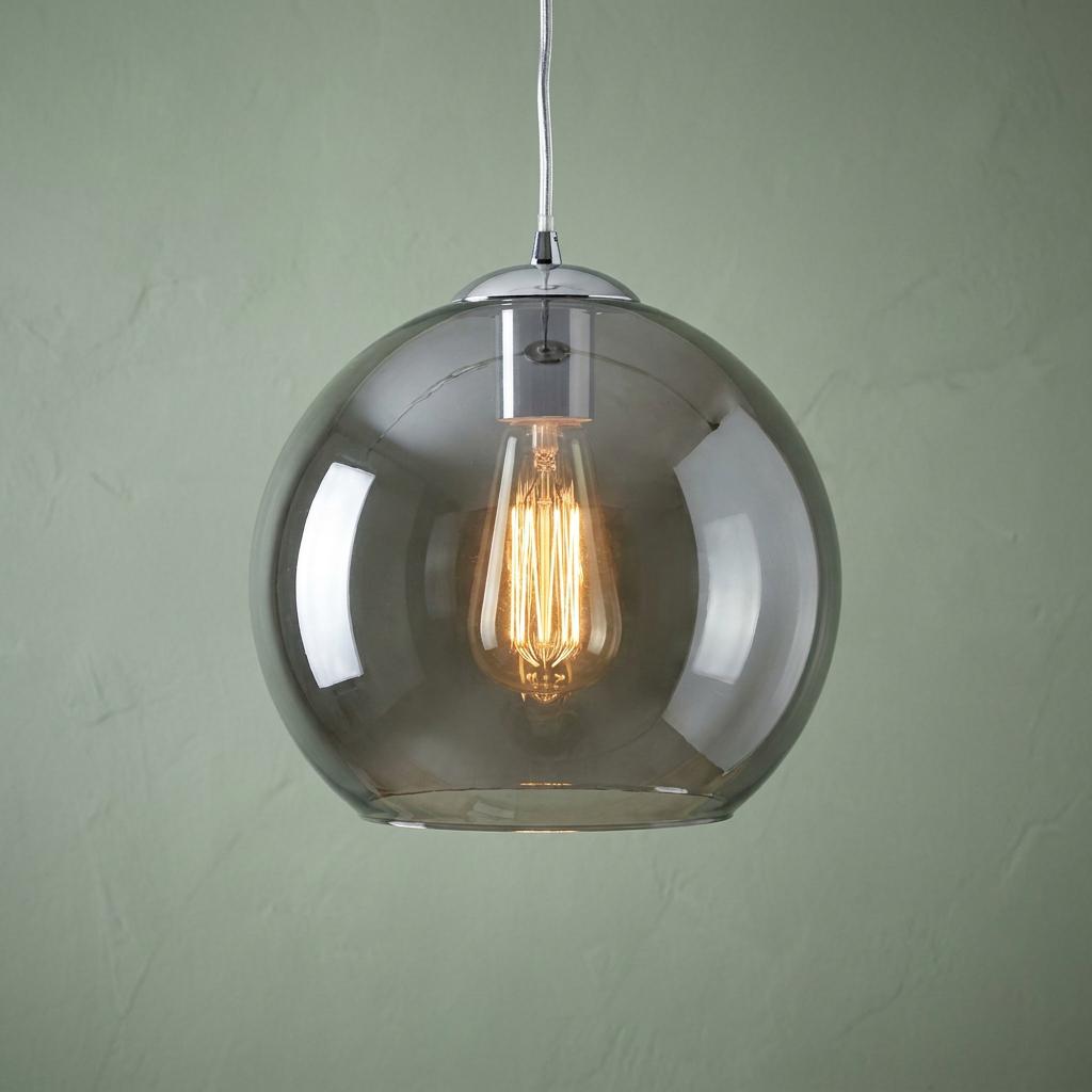 Round smoked glass pendant light with a glowing vintage bulb hanging against a pale green wall.