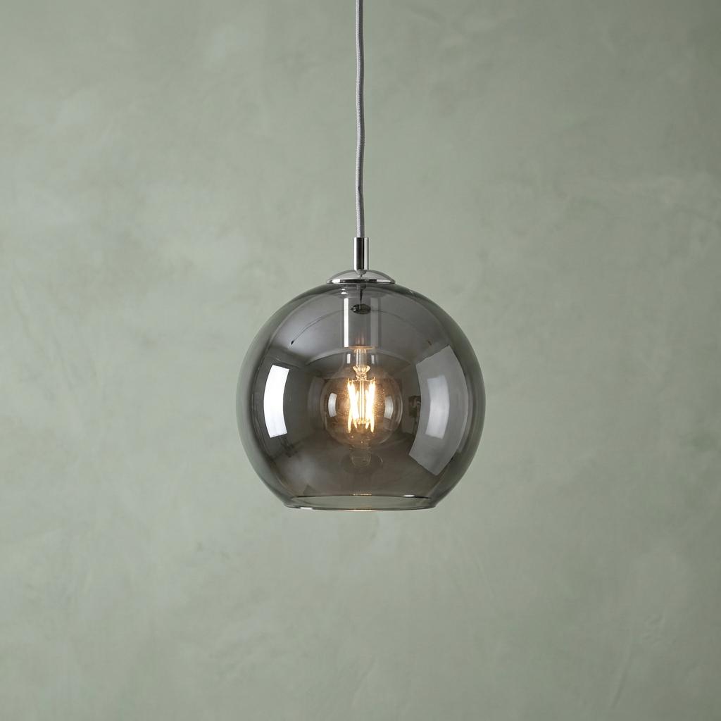 A spherical smoked glass pendant light with a lit filament bulb hanging against a pale green textured wall.