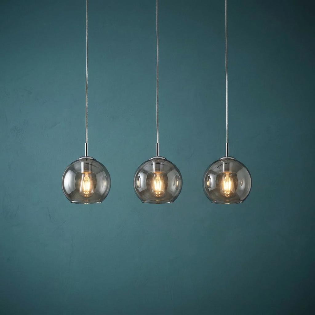 Three modern pendant lights with smoked glass globe shades and glowing bulbs hanging against a teal wall.