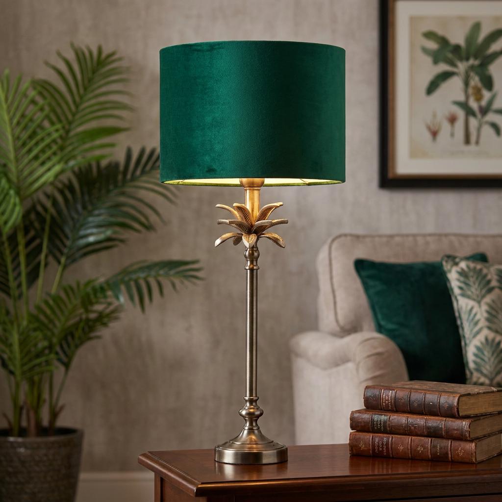 Antique nickel palm table lamp with a green velvet shade glowing in a living room setting next to old books.
