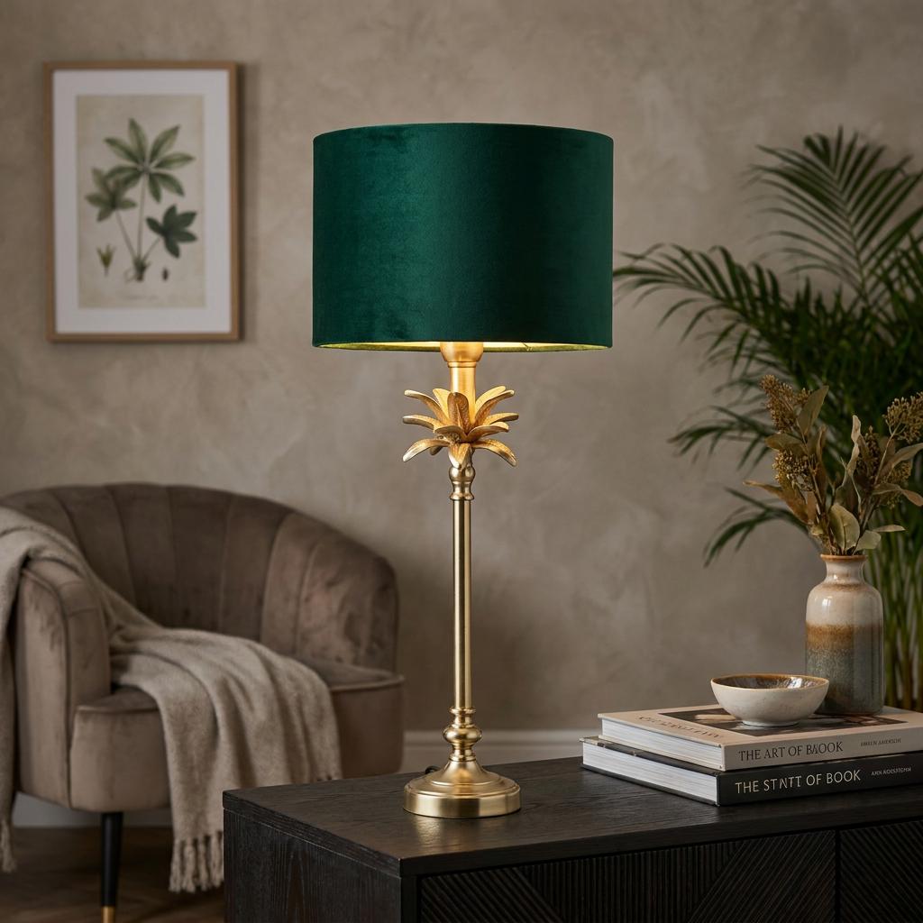 Satin brass palm table lamp with a green velvet drum shade sitting on a dark wooden cabinet in a living room.