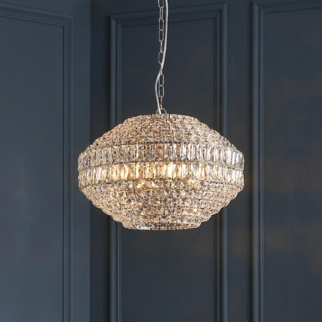 Lit Beatrice 5 light crystal glass and chrome pendant hanging against a dark blue panelled wall.