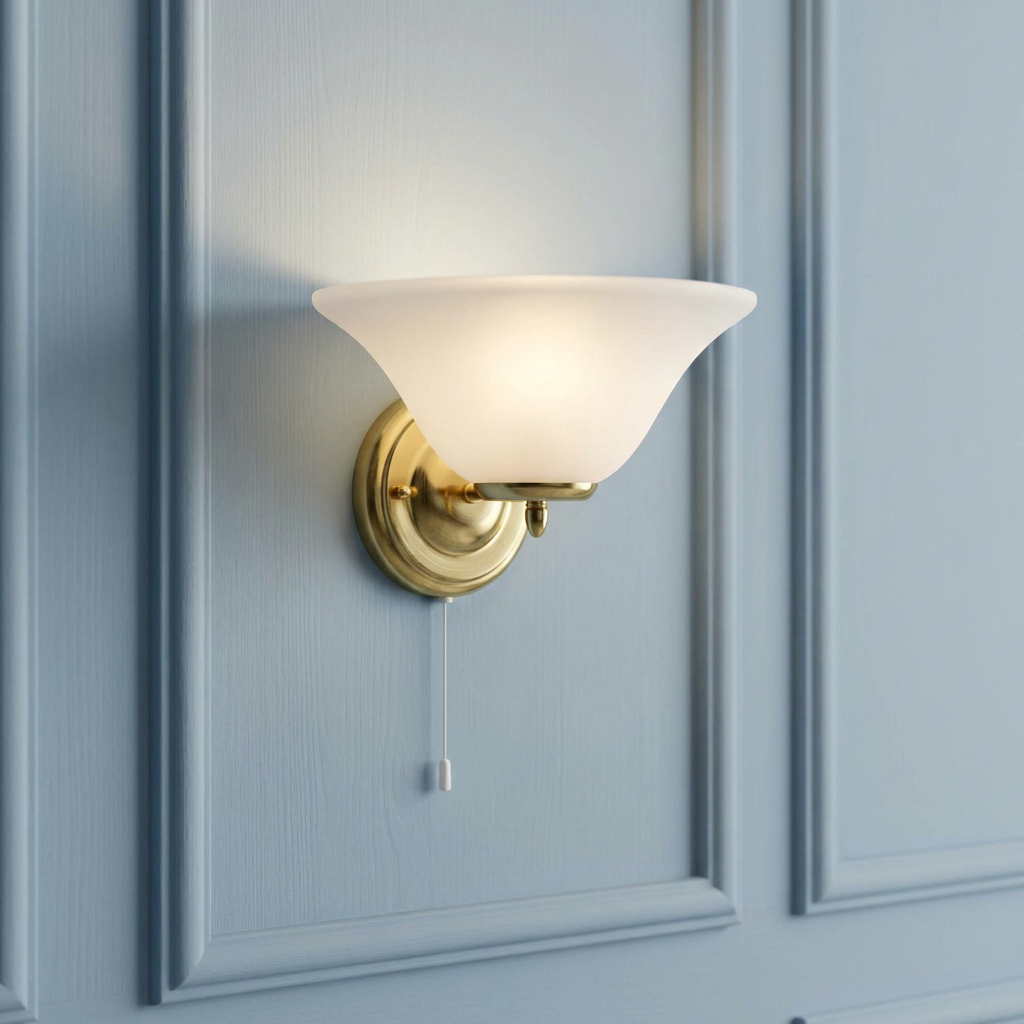 A brass wall light with a frosted alabaster glass shade and pull cord, mounted on a blue paneled wall.