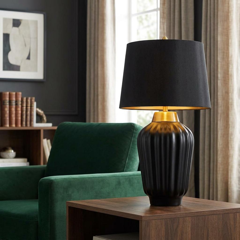 Black and brushed brass table lamp with a ribbed ceramic base on a wooden side table in a modern living room.