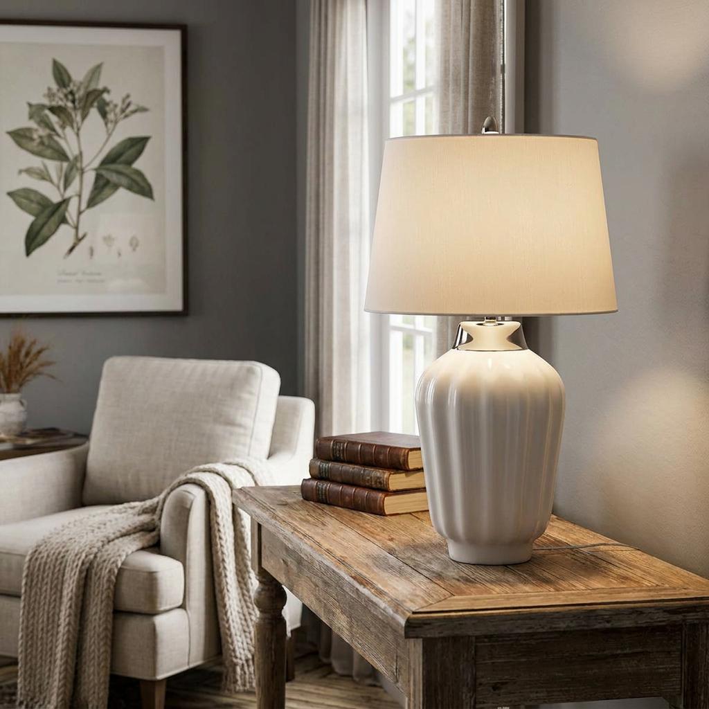 White ribbed ceramic table lamp with polished nickel accents on a wooden side table in a cozy, neutral living room.