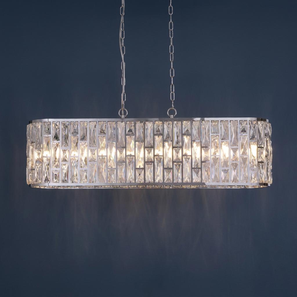 Modern oval pendant light featuring clear rectangular crystals and a polished chrome finish on a dark blue wall.