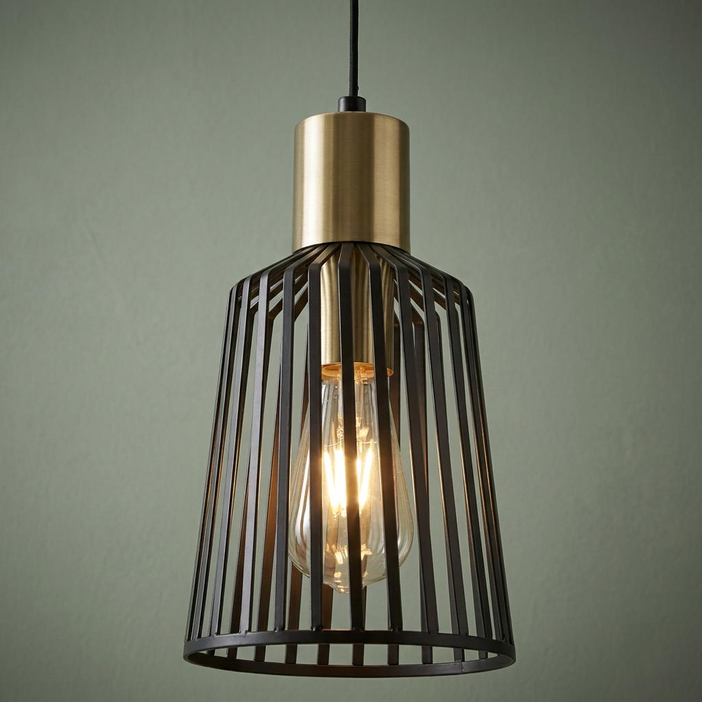 Black birdcage pendant light with gold accents and a glowing Edison bulb against a green wall.