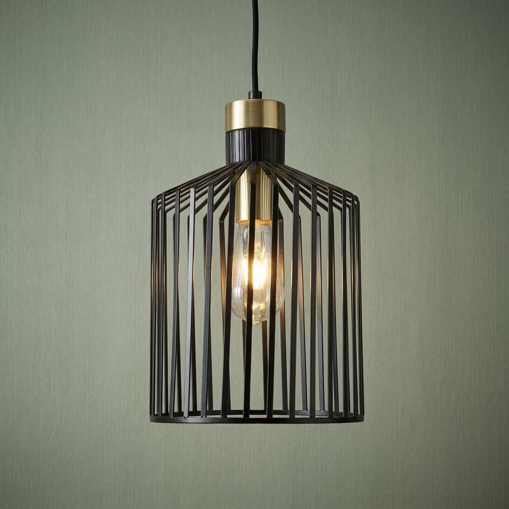 A black slatted birdcage pendant light with a gold accent and lit Edison bulb against a green wall.