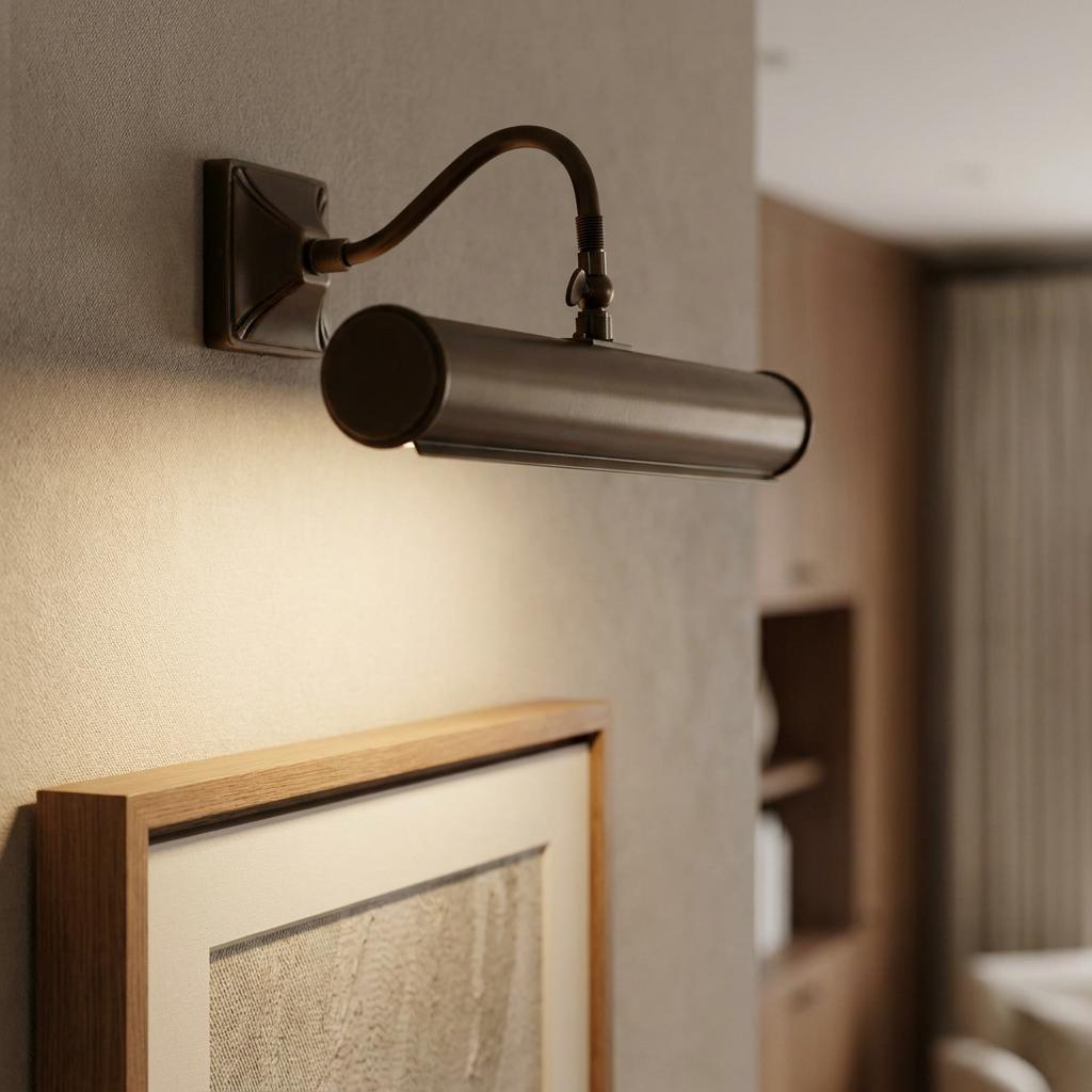 Antique bronze picture light mounted on a wall above a framed picture, casting a warm glow downwards.
