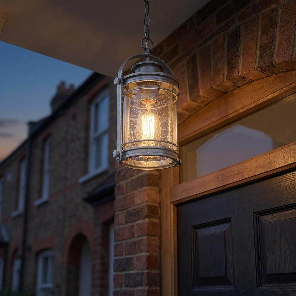 Booker 1 Light Small Outdoor Chain Lantern with seeded glass and a warm Edison bulb hanging on a brick porch at dusk.