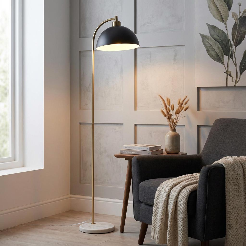 A brass task floor lamp with a black dome shade and white marble base in a cozy living room nook.