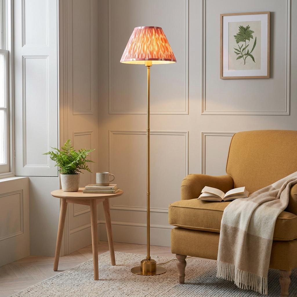 Brass floor lamp with a coral pink ikat shade standing next to a yellow armchair in a cozy paneled living room.