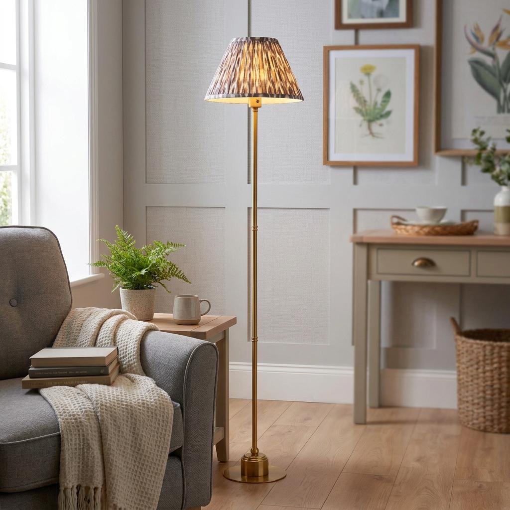 A lit Burley brass floor lamp with a grey ikat shade in a cozy living room next to a grey armchair.