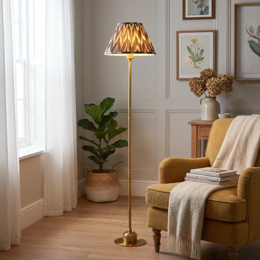 Brass floor lamp with a pearl grey zigzag shade standing next to a yellow armchair in a cozy living room.
