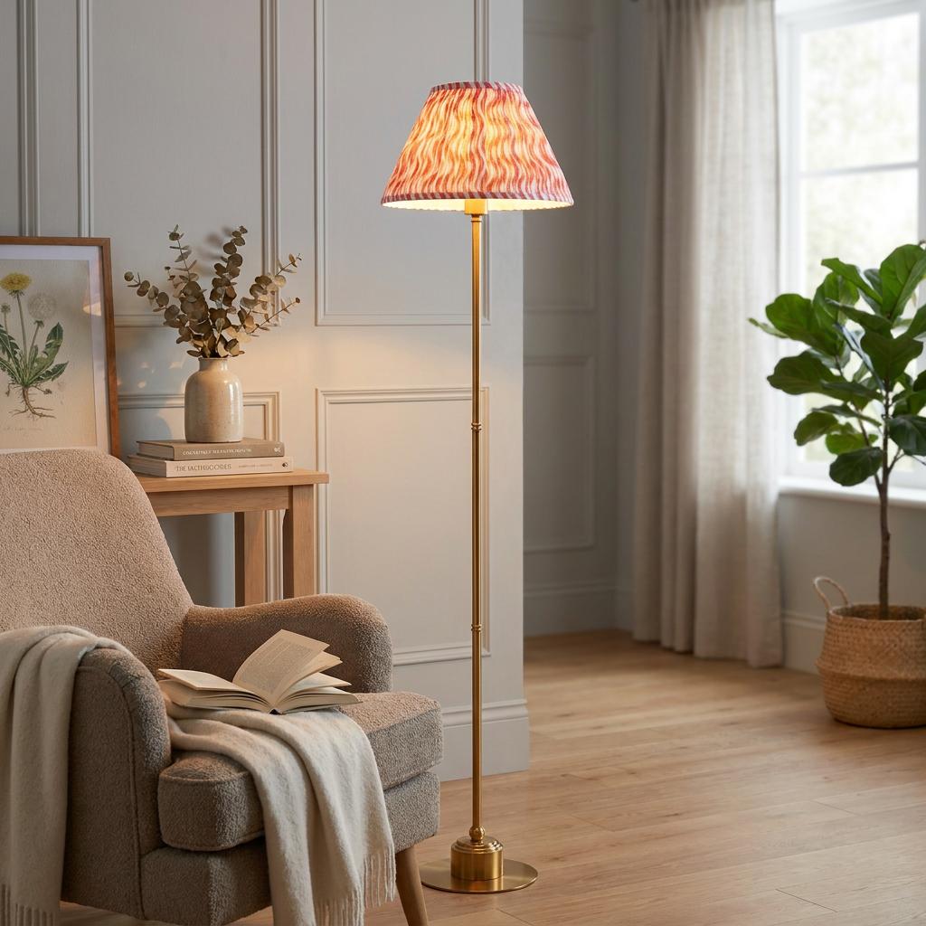 Brass floor lamp with a coral pink ripple shade illuminates a cozy living room with a plush armchair.