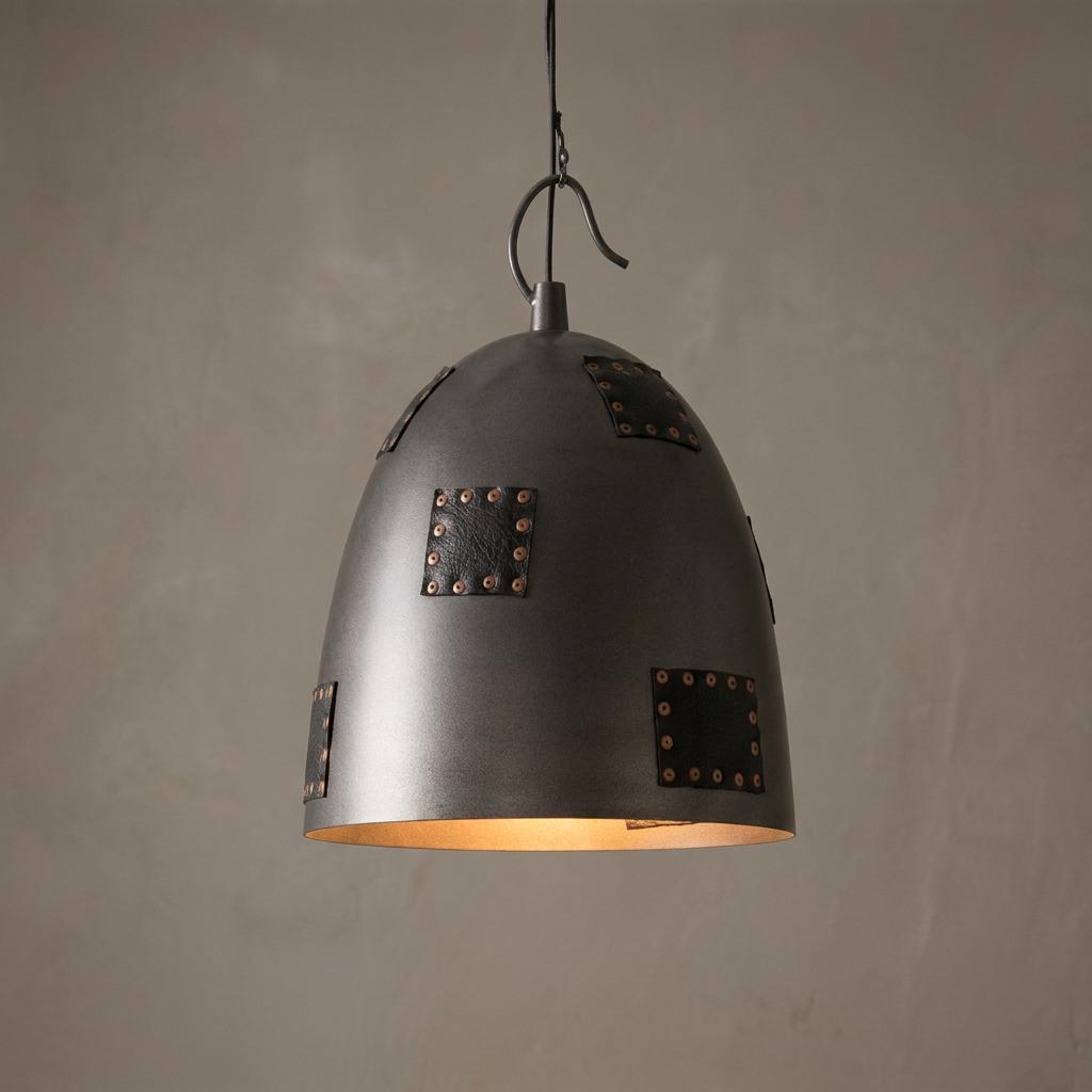 Industrial dome pendant light with riveted leather patches and a warm interior glow against a grey wall.