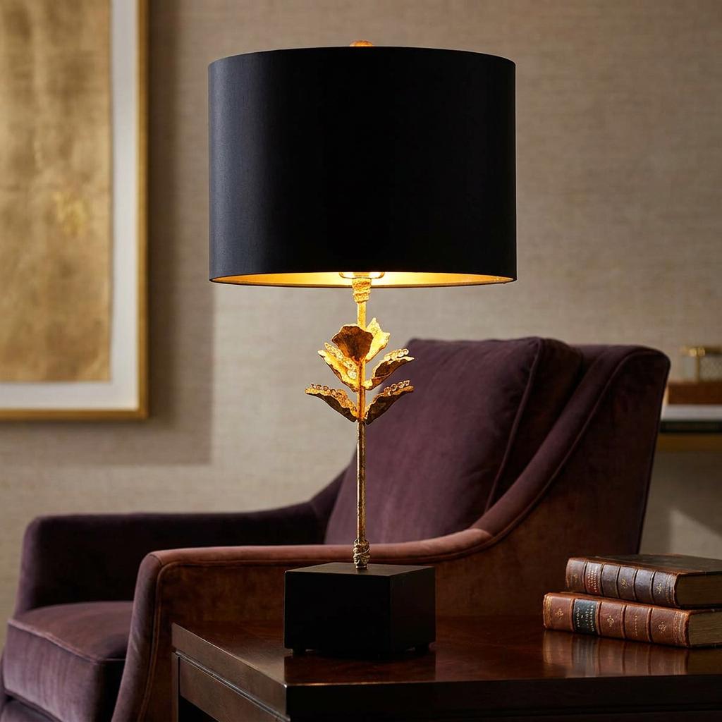 Camilia antique gold table lamp with a black shade sits on a wooden side table next to a purple velvet chair.