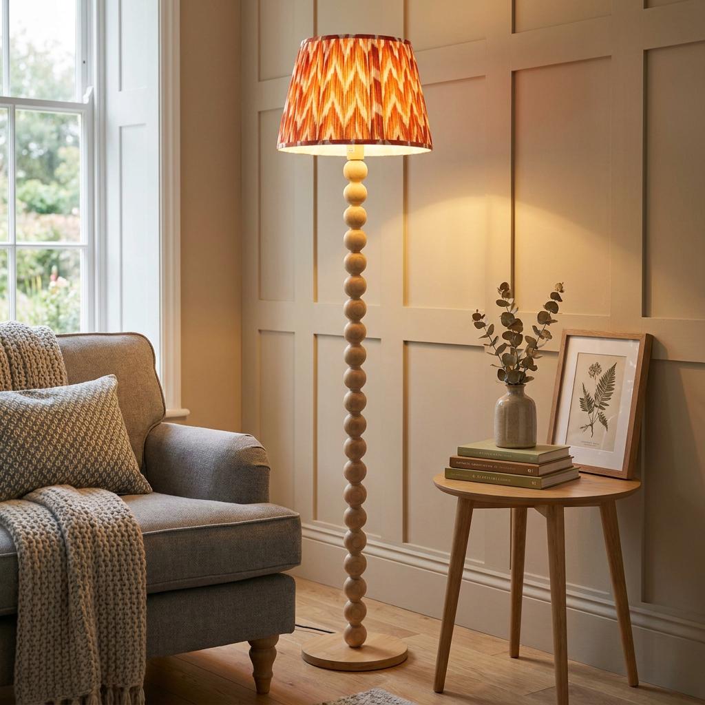 A bobbin-style floor lamp with an orange zigzag shade stands in a cozy living room beside a grey armchair.