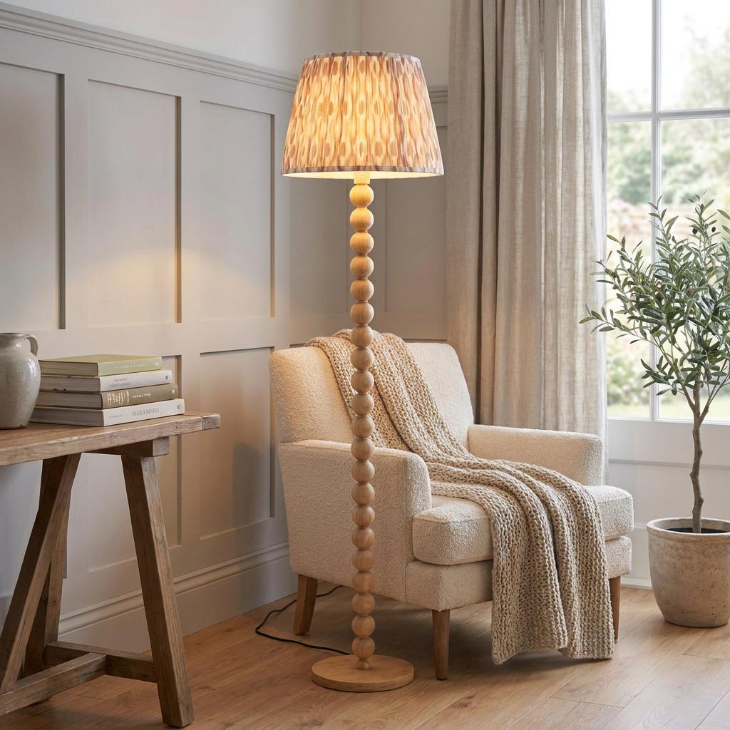 Bobbin-style cane floor lamp with a neutral ikat shade standing beside a cream armchair in a bright living room.