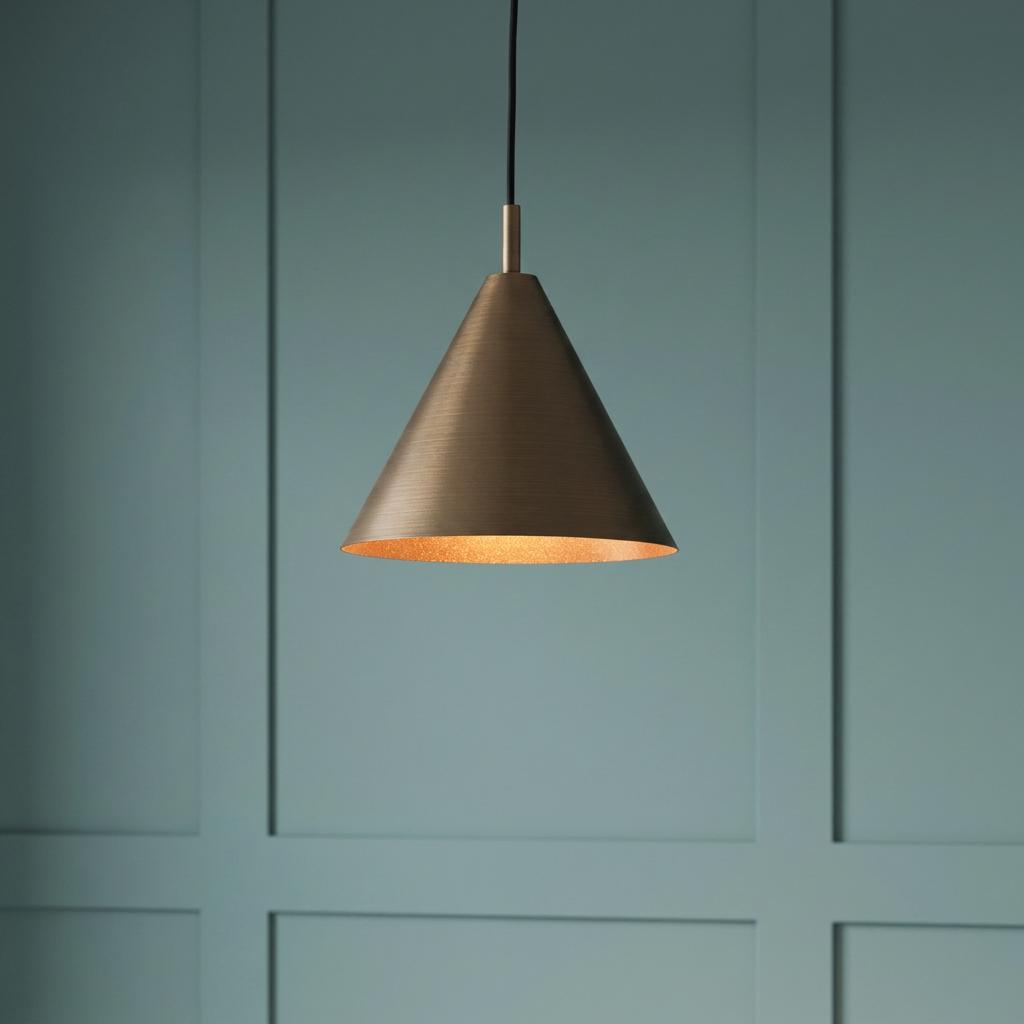 Cone-shaped bronze pendant light with a warm interior glow hanging against a teal paneled wall.