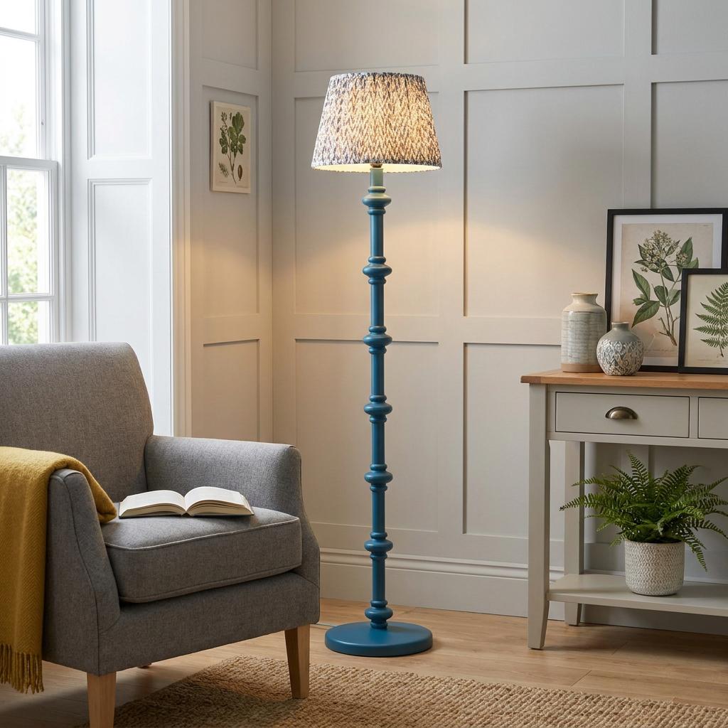 Illuminated blue bobbin floor lamp with a patterned pearl grey shade in a neutral living room by a grey armchair.