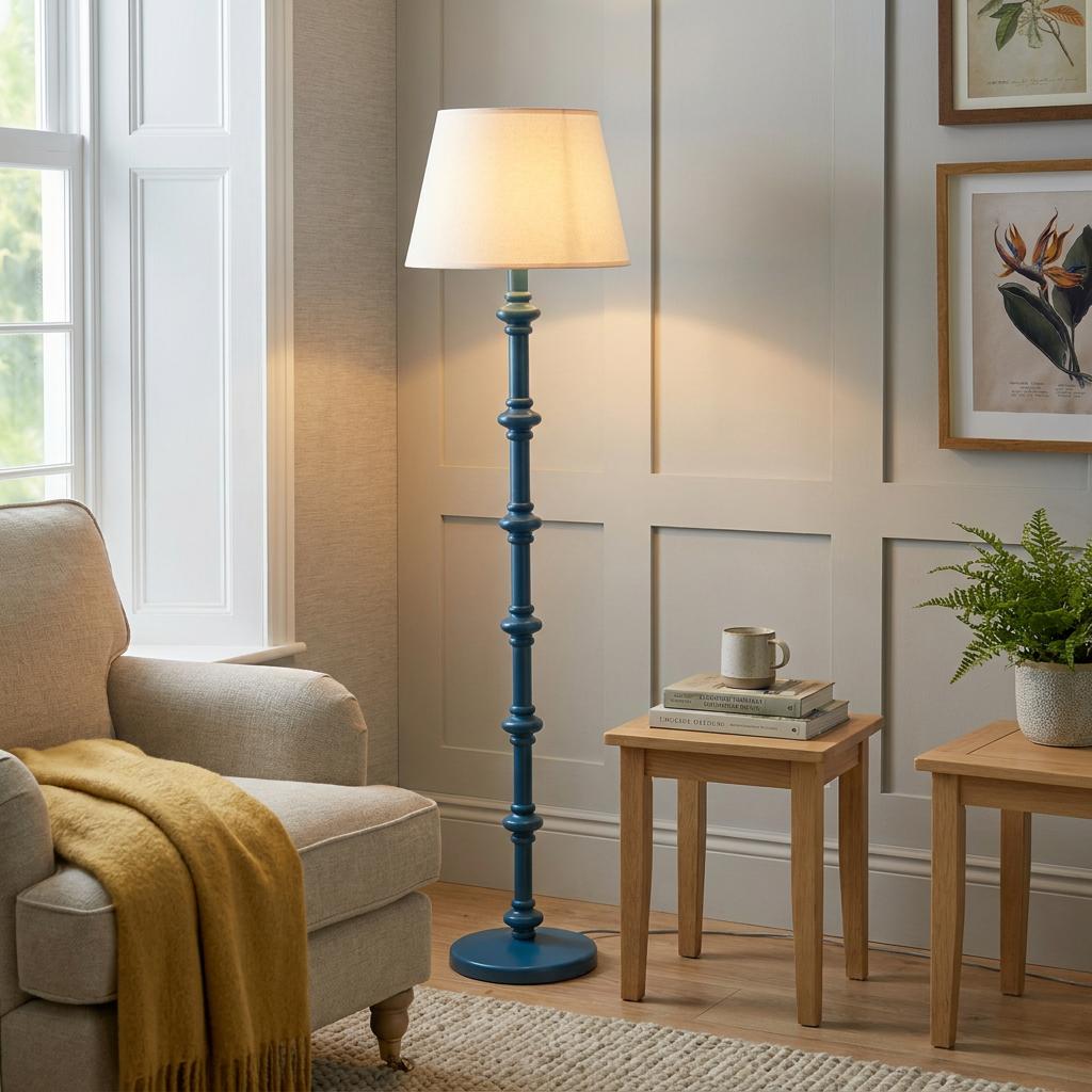 Blue spindle floor lamp with a white shade illuminates a cozy living room next to a beige armchair.