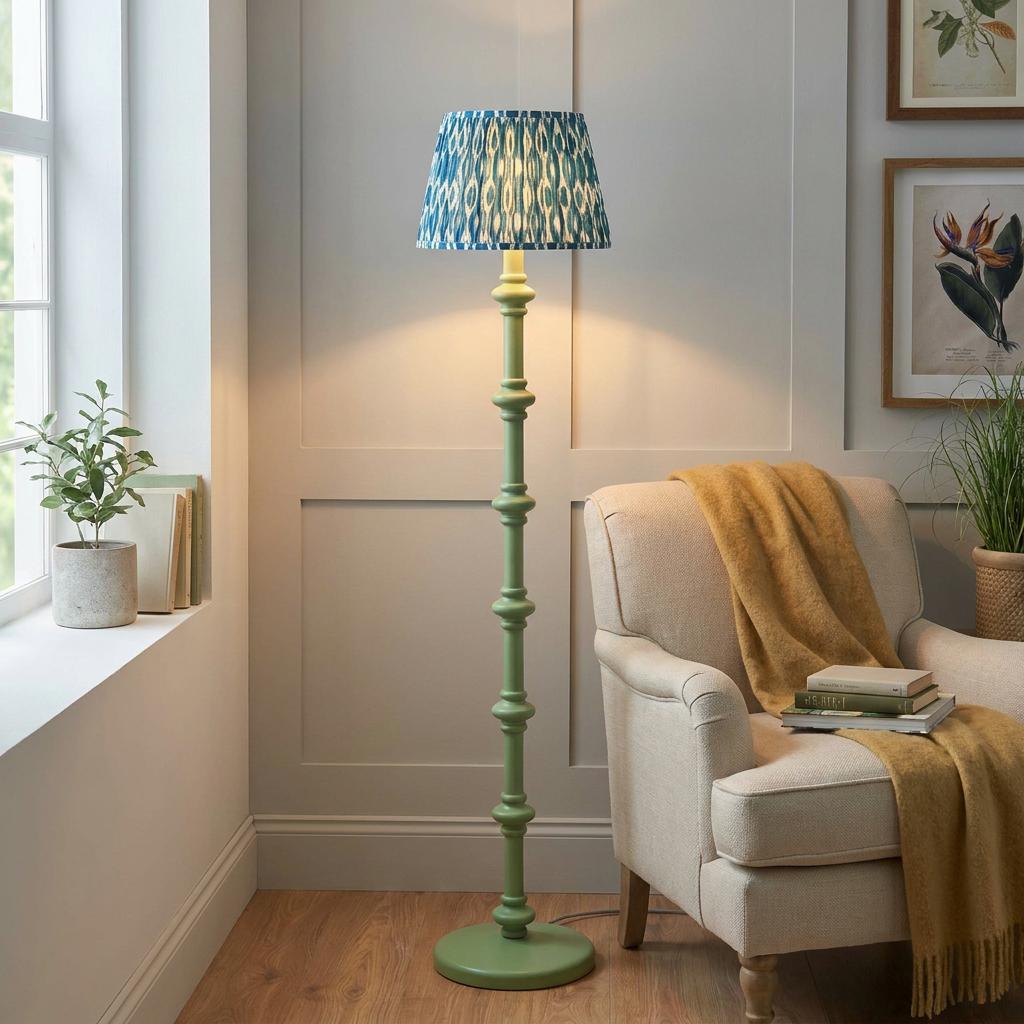Green bobbin floor lamp with a blue ikat shade illuminates a cozy living room nook with a cream armchair.