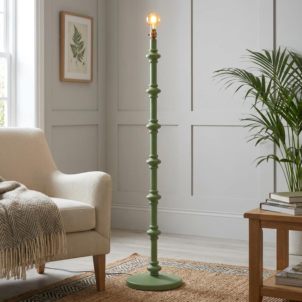 Sage green spindle floor lamp base with an Edison bulb in a living room next to a cream chair and green plant.