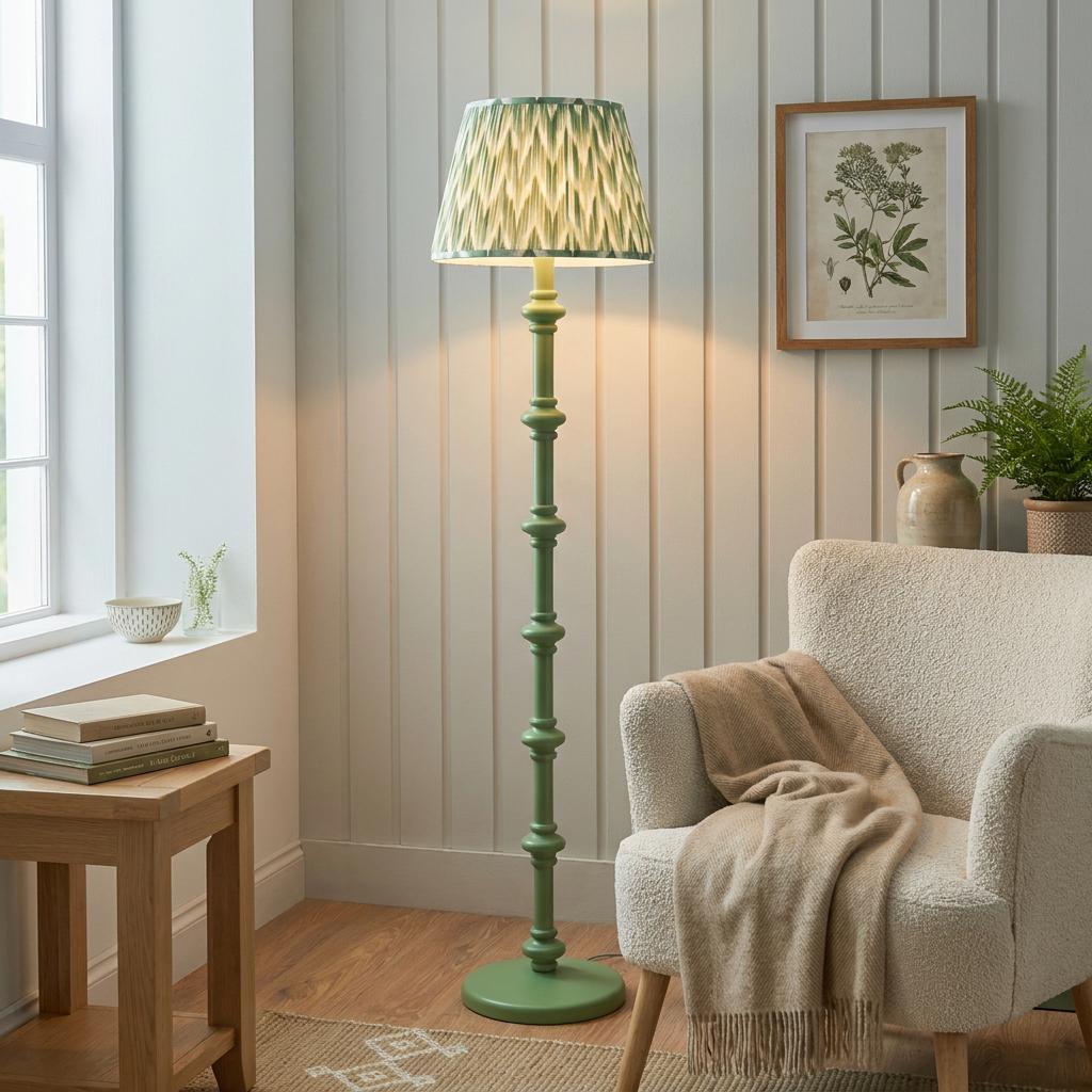 Sage green turned wood floor lamp with a green zigzag ikat shade in a cozy living room corner next to a boucle chair.