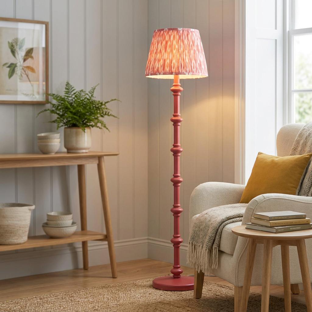Coral pink turned floor lamp with a patterned ikat shade illuminating a cozy living room corner with an armchair.