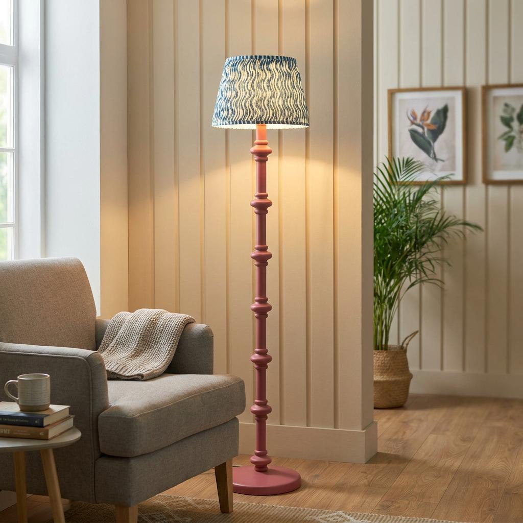 A pink bobbin-style floor lamp with a blue and white patterned lampshade in a cozy living room setting.