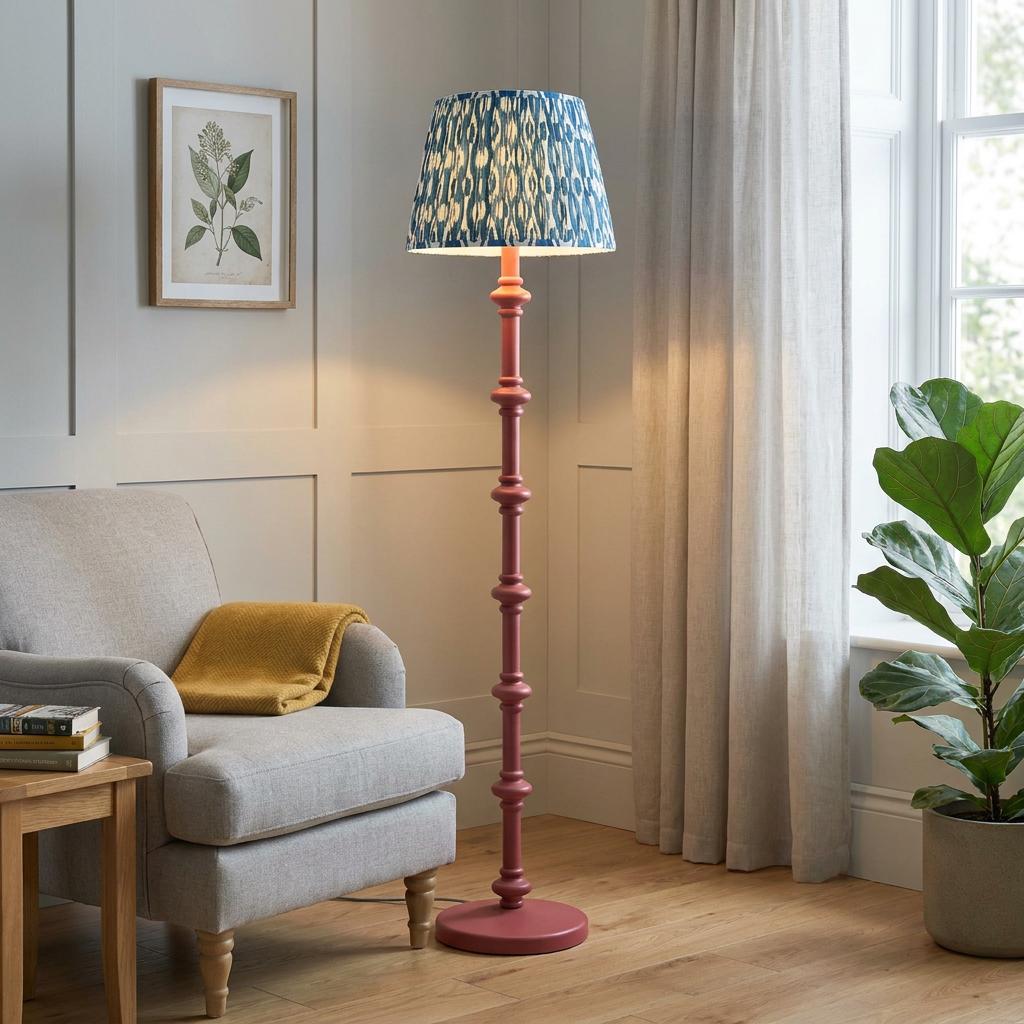 Pink bobbin floor lamp with a blue ikat shade beside a grey armchair in a well-lit living room.