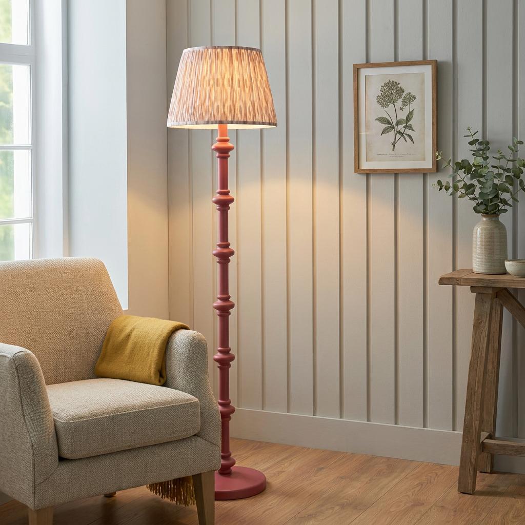 Pink wooden floor lamp with an ikat shade standing next to an armchair in a room with grey wall paneling.